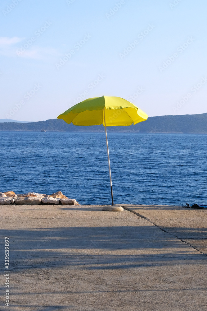 Yellow beach umbrella on summer coast. Sea beach with sun umbrella is waiting for tourists on Sunset. Happy summer vacations concept. Vertical view.