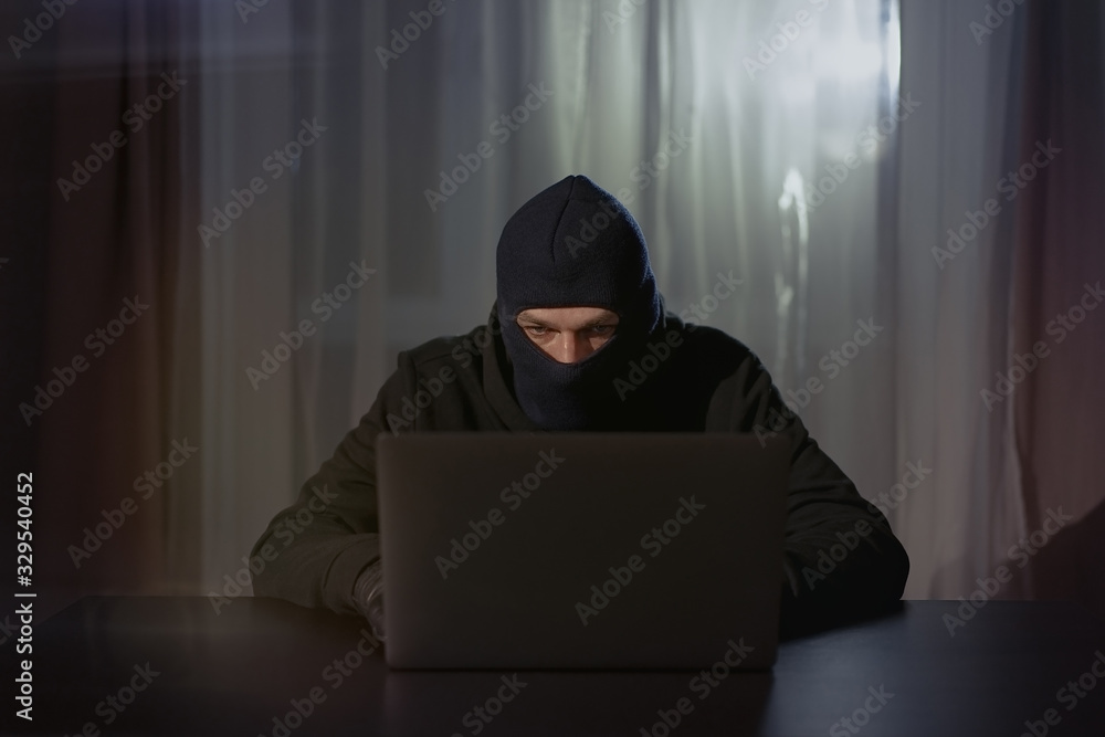 Male hacker in the hood in a dark room using computer virus program for cyber attack. Hackers and cyber security concept Male hacker in the hood in a dark room using computer virus program for cyber attack. Hackers and cyber security concept