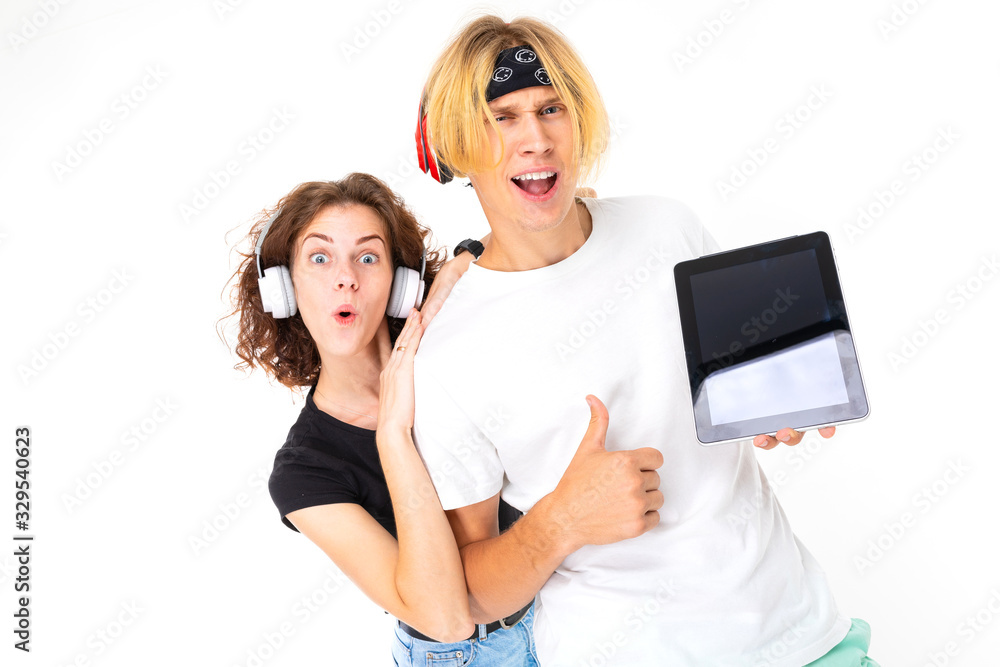 Stylish caucasian blonde man and young woman shows tablet and listen to music isolated on white background Stylish caucasian blonde man and young woman shows tablet and listen to music isolated on white background