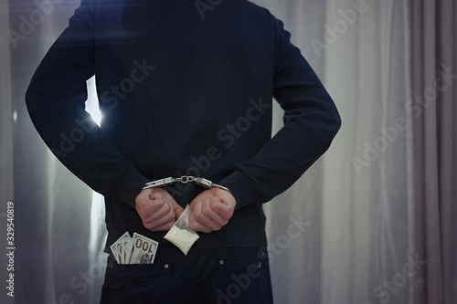 Arrested man handcuffed hands holding bribe money behind back 