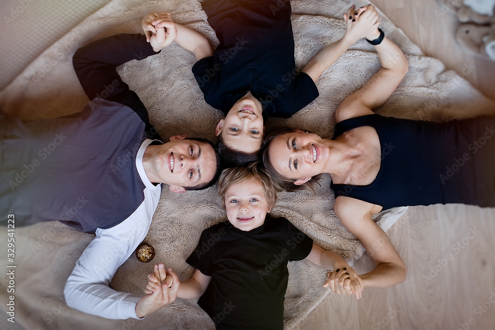 Happy family looking at camera and smiling while lying on the floor at home. Top view   