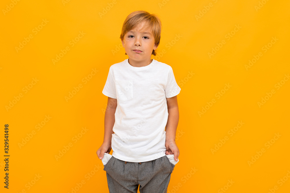 Cute little boy in t-shirt and trousers holds his hands in pockets isolated on yellow background Cute little boy in t-shirt and trousers holds his hands in pockets isolated on yellow background