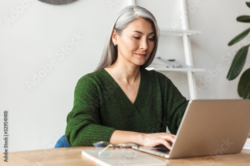 Foto Photo of gray-haired focused businesswoman typing on laptop
