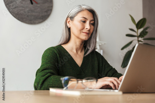 Photo of gray-haired focused businesswoman typing on laptop