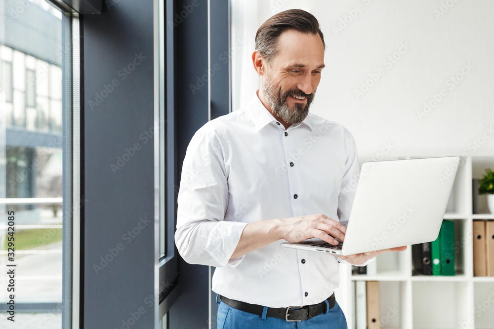 Fototapeta premium Photo of bearded smiling businessman in white shirt typing on laptop