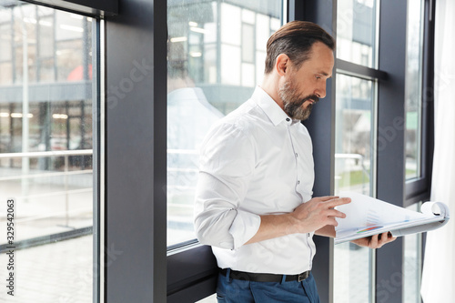 Photo of bearded focused businessman in white shirt examining documents