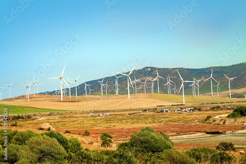 Windmills wind turbines farm power generators against landscape against blue sky in beautiful nature landscape for production of renewable green energy. Friendly industry to environment.