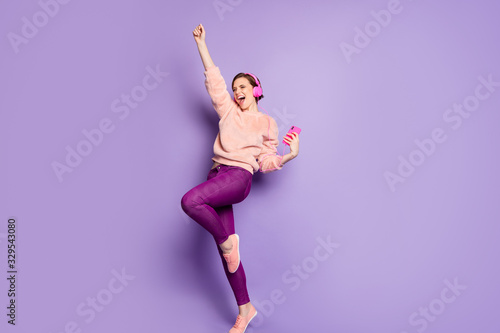 Full length photo of pretty lady hold telephone modern earphones on ears listen youth music dance students party wear casual stylish pink jumper pants isolated purple color background