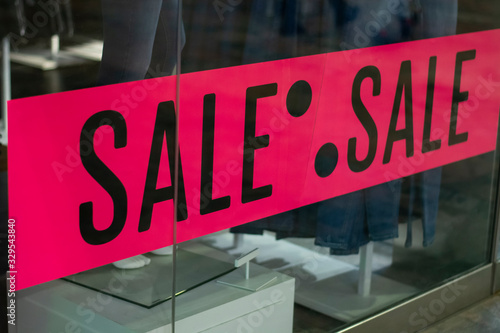 Sale advertisement at a clothing store. Pink poster sign with the word Sale at the entrance. Shop window on the outside of fashion store display poster sticker.
