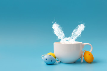 Steam in rabbit ears shape from coffee cup decorated easter colored eggs. Morning drink. Easter celebration concept. Copy space