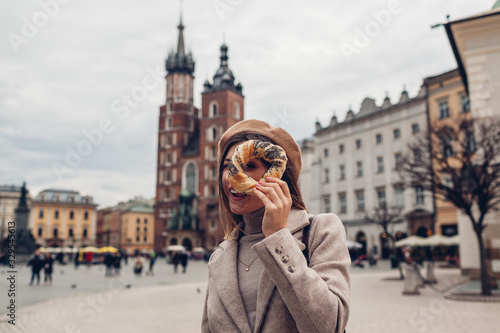 Tourist woman holding bagel obwarzanek traditional polish cuisine snack on Market square in Krakow. Travel Europe
