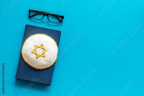 Jewish Kippah Yarmulkes hats with Star of David on Prayer book. Religion Judaisim symbols on blue table. Top view, space for text photo