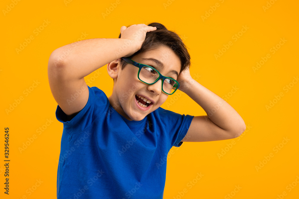 young boy in a blue t-shirt with glasses holds his head on a yellow background young boy in a blue t-shirt with glasses holds his head on a yellow background