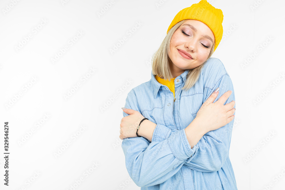 stylish blonde girl in casual look hugs herself on a white background