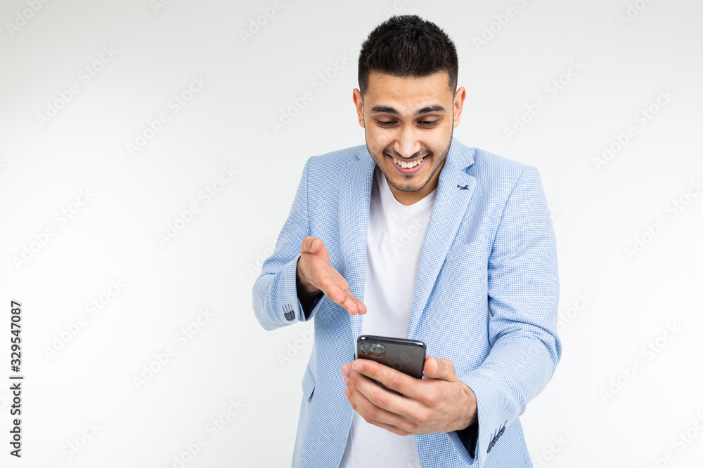 smiling stylish brunette man in a blue jacket looks at the phone on a white background smiling stylish brunette man in a blue jacket looks at the phone on a white background