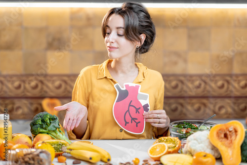 Cuadro en lienzo Woman holding human heart model with variety of healthy fresh food on the table