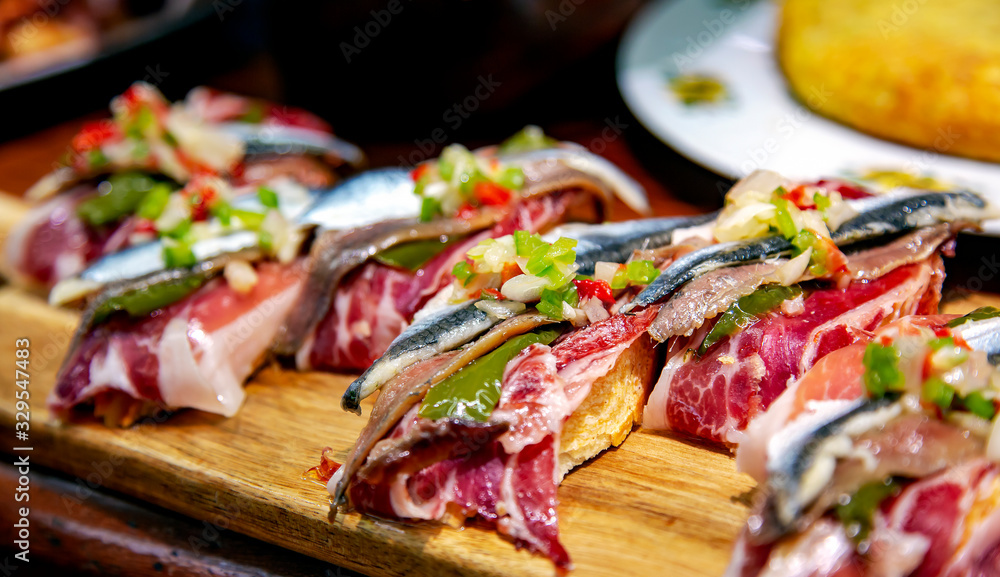 Naklejka premium Apetyczne hiszpańskie tapas z jamonem, anchois i zielonymi warzywami na drewnianej tacy zbliżenie w San Sebastian, Donostia, Hiszpania