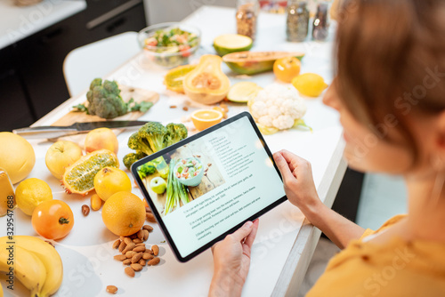 Woman looking on the digital recipe, using touchscreen tablet while cooking healthy meal on the kitchen at home, close-up view on the screen photo