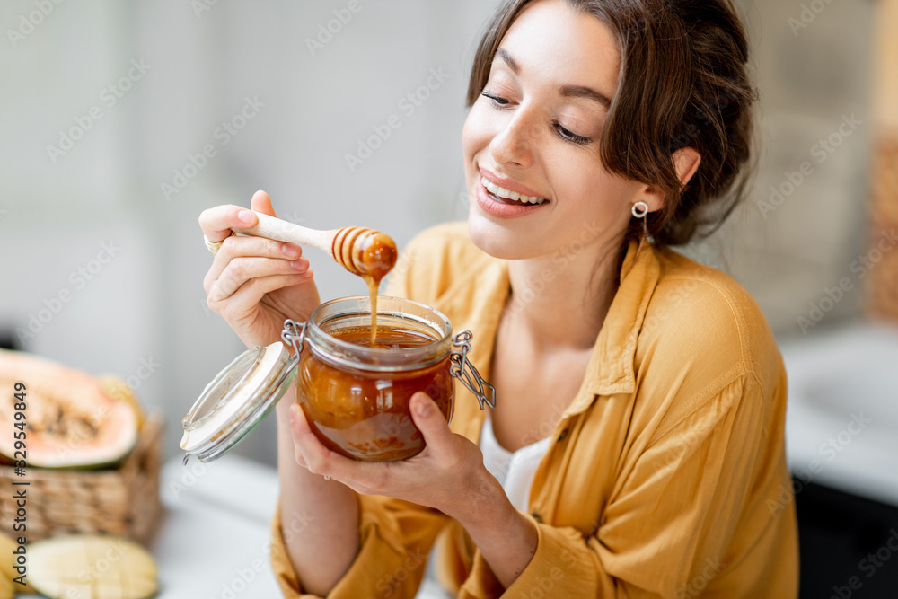 Portrait of a young and cheerful woman with a jar full of sweet honey on the kitchen at home Portrait of a young and cheerful woman with a jar full of sweet honey on the kitchen at home