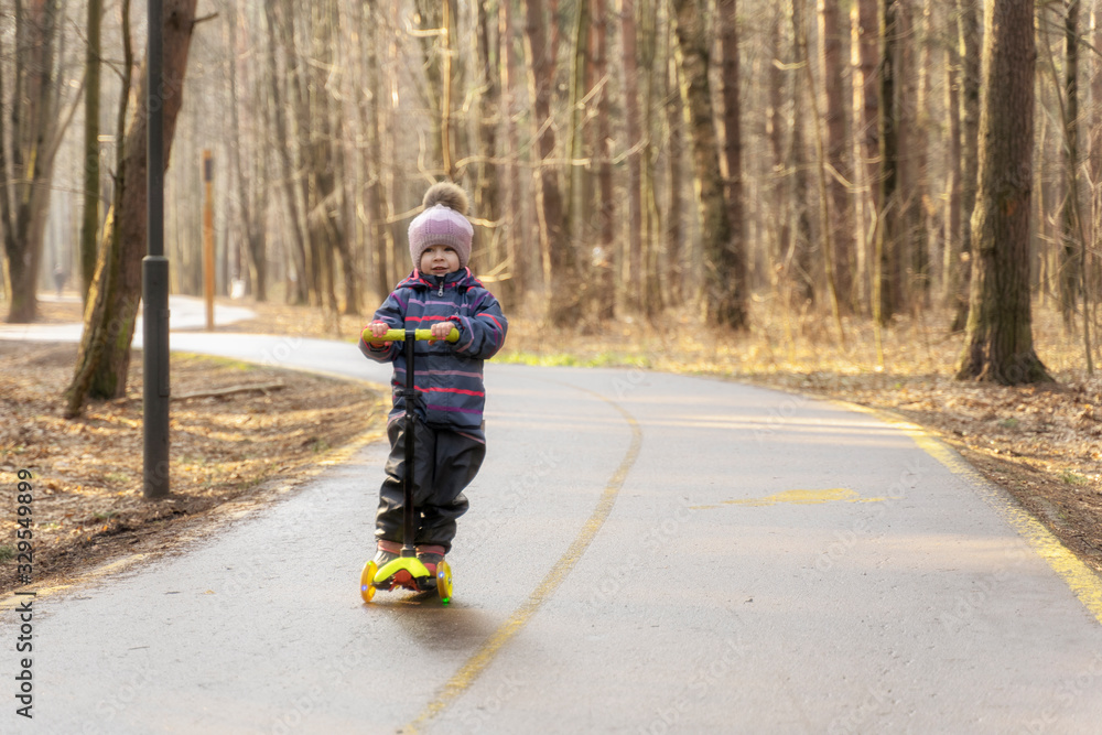 Obraz premium a child races on a scooter along an asphalt road in a spring park