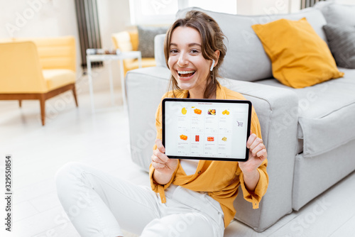 Young and cheerful woman showing a digital tablet screen with launched online store, shopping online at home. Concept of buying online using mobile devices
