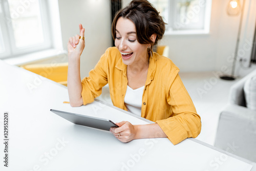 Young and cheerful woman using a digital tablet while sitting relaxed at home. Concept of a leisure activities with mobile devices at home photo