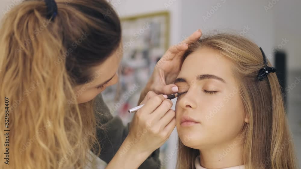 A professional makeup artist applying makeup to the woman by eye pencil at a salon A professional makeup artist applying makeup to the woman by eye pencil at a salon