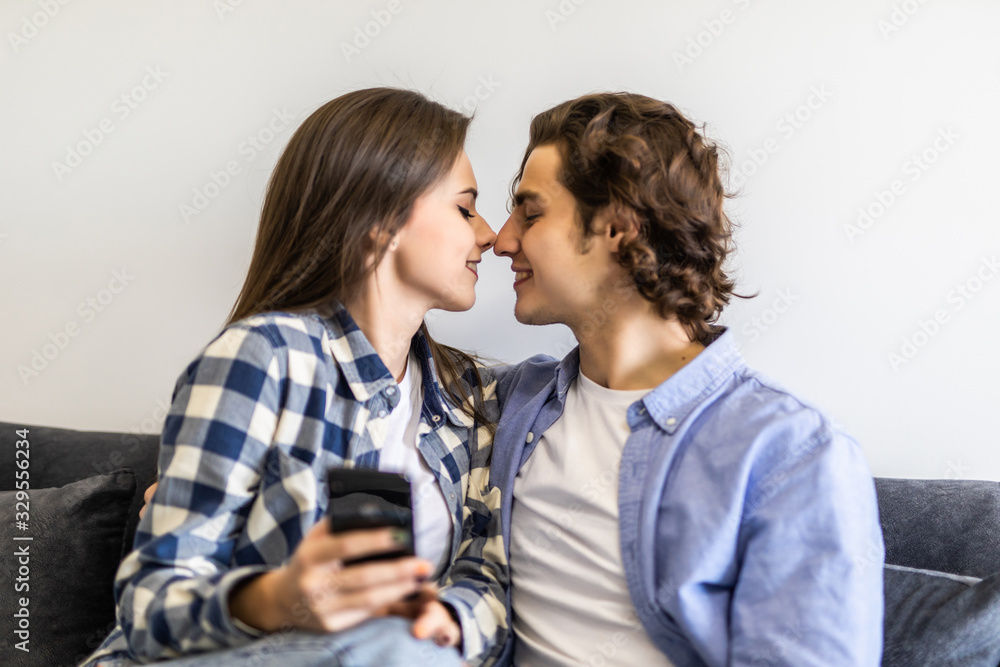 Young couple or marriage sharing a smart phone to watch media content sitting on a couch at home Young couple or marriage sharing a smart phone to watch media content sitting on a couch at home