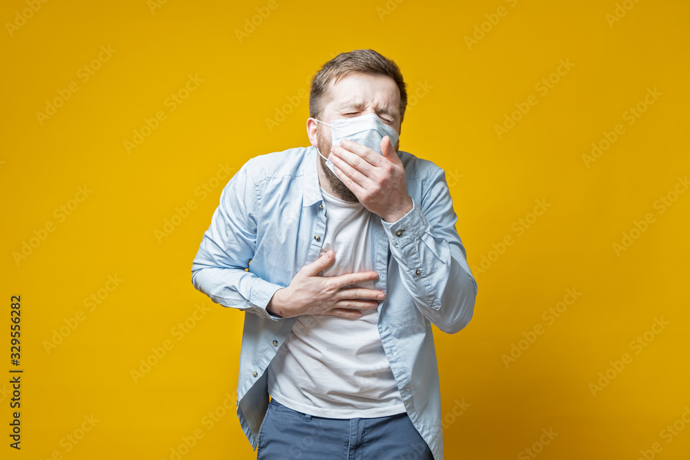 Man in a medical mask coughs, covering mouth with palm and holds hand on chest. Concept of the spread of the virus. Man in a medical mask coughs, covering mouth with palm and holds hand on chest. Concept of the spread of the virus.