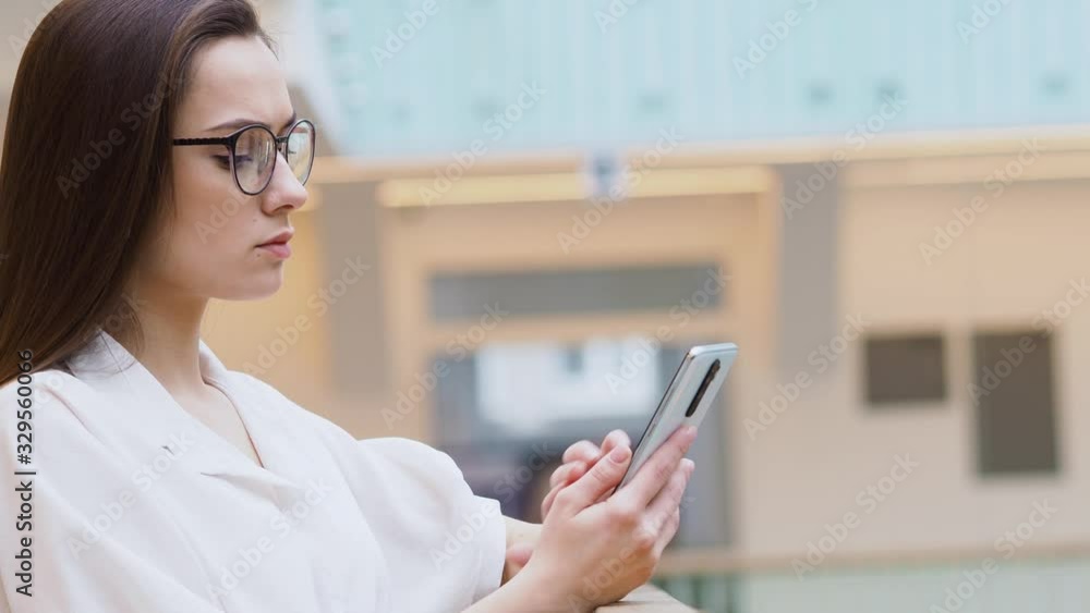 young woman in stylish business clothes and glasses uses a smartphone to communicate with a chatbot. The girl pokes at the touch screen young woman in stylish business clothes and glasses uses a smartphone to communicate with a chatbot. The girl pokes at the touch screen