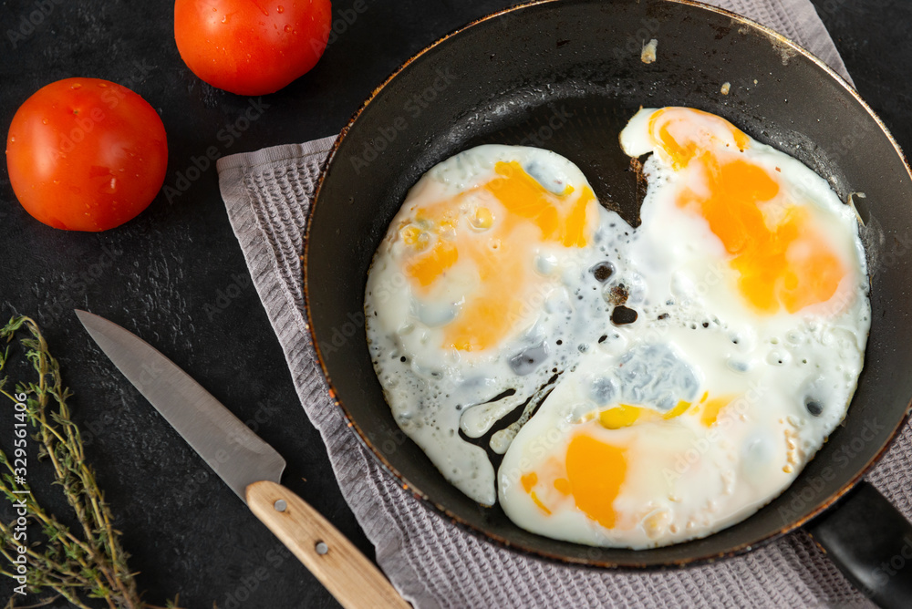 fried eggs in a frying pan , tomatoes, towel, knife, thyme, shell on a black fried eggs in a frying pan , tomatoes, towel, knife, thyme, shell on a black