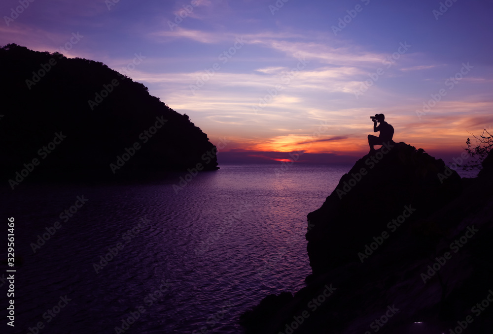 Silhouette of photographer using camera on the top of a rock by the sea , Twilight  sky sunset