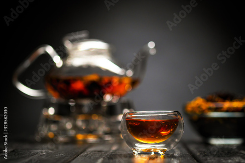 Horizontal photo of the tea set on a black background. Glass transparent teapot and cup. Black leaf tea.