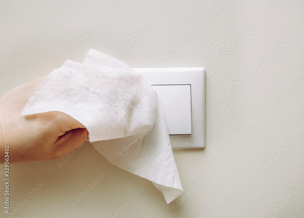 Close up view of woman hand using antibacterial wet wipe for disinfecting home room electric switch on wall. - obrazy, fototapety, plakaty 