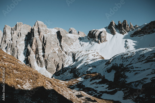 Scenic ridge of mountains in North Italy with the rest of the snow beneath them in shadow in valley during the sunny spring afternoon with the clear blue sky in the background