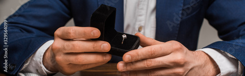 Cropped view of jewelry appraiser holding box with jewelry ring at table isolated on grey, panoramic shot photo
