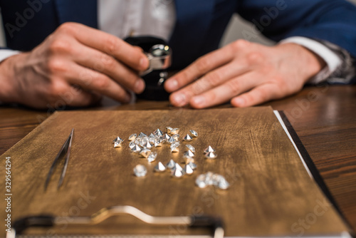 Selective focus of gemstones on board and jewelry appraiser working at table isolated on grey