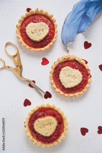 Crostatine alle fragole, con pezzettino di pasta all'interno. Sfondo bianco con cuori, un paio di forbici dorate e un foulard blu photo