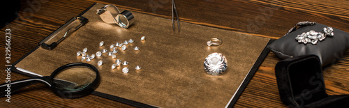 Panoramic shot of gemstones and jewelry with magnifying glasses on board on wooden table photo