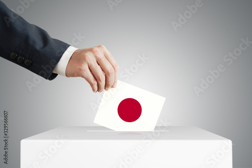 Man putting a voting ballot into a box with Japanese flag. photo