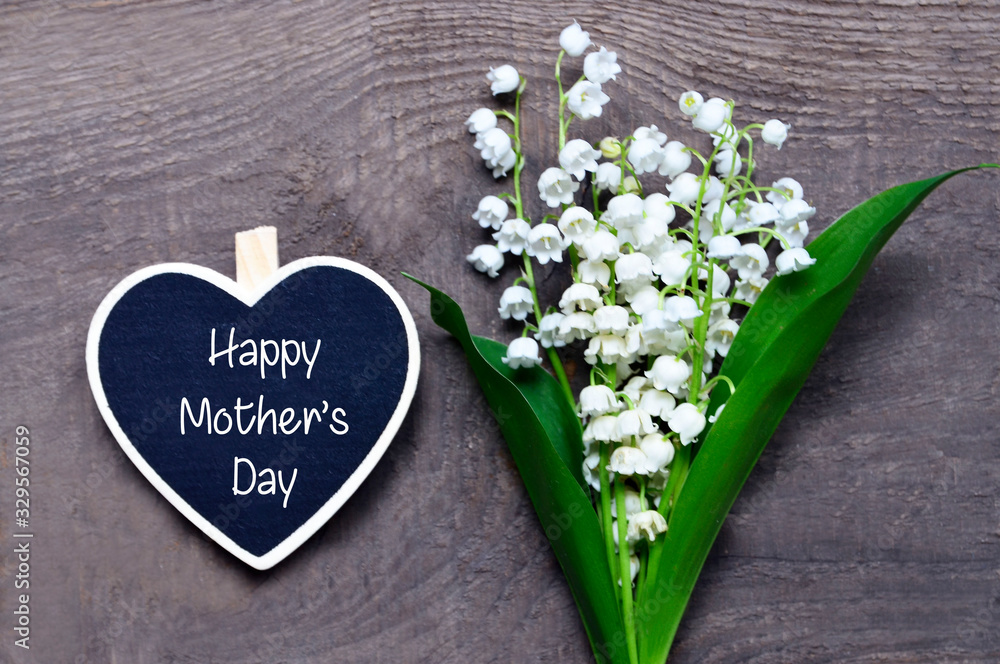 Bouquet of lilies of the valley and decorative heart with Happy Mother's Day text on wooden background.Lily-of-the-valley flowers. Spring festive concept.Selective focus. Bouquet of lilies of the valley and decorative heart with Happy Mother's Day text on wooden background.Lily-of-the-valley flowers. Spring festive concept.Selective focus.