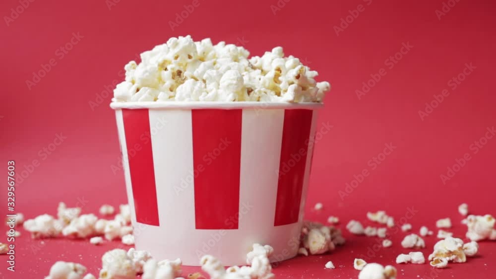 popcorn is poured on top of a striped cardboard box on a red background. American food background. Fast food. popcorn is poured on top of a striped cardboard box on a red background. American food background. Fast food.