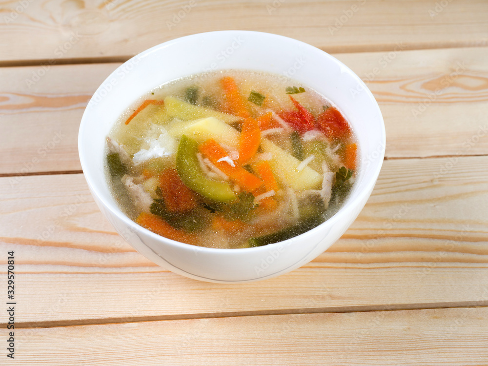 Chicken soup with vermicelli and vegetables. Soup in a white round bowl on a wooden surface. Side view Chicken soup with vermicelli and vegetables. Soup in a white round bowl on a wooden surface. Side view