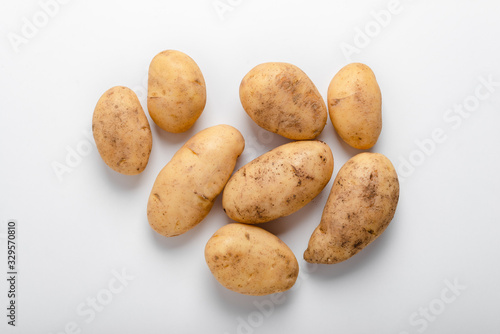 Heap of raw unwashed yellow potatoes over white background, top view