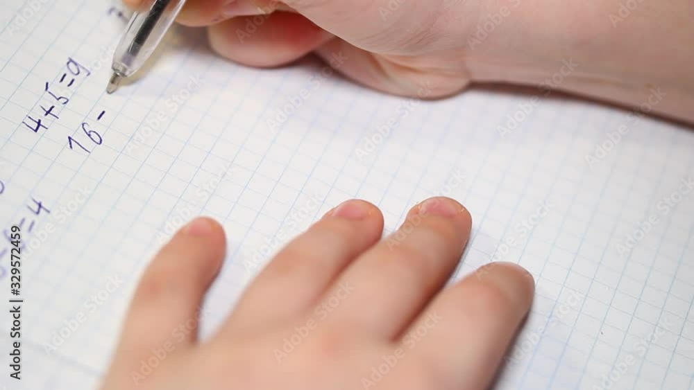 The child does school homework, solves arithmetic examples and writes them in a notebook. Affordable education concept. The child does school homework, solves arithmetic examples and writes them in a notebook. Affordable education concept.