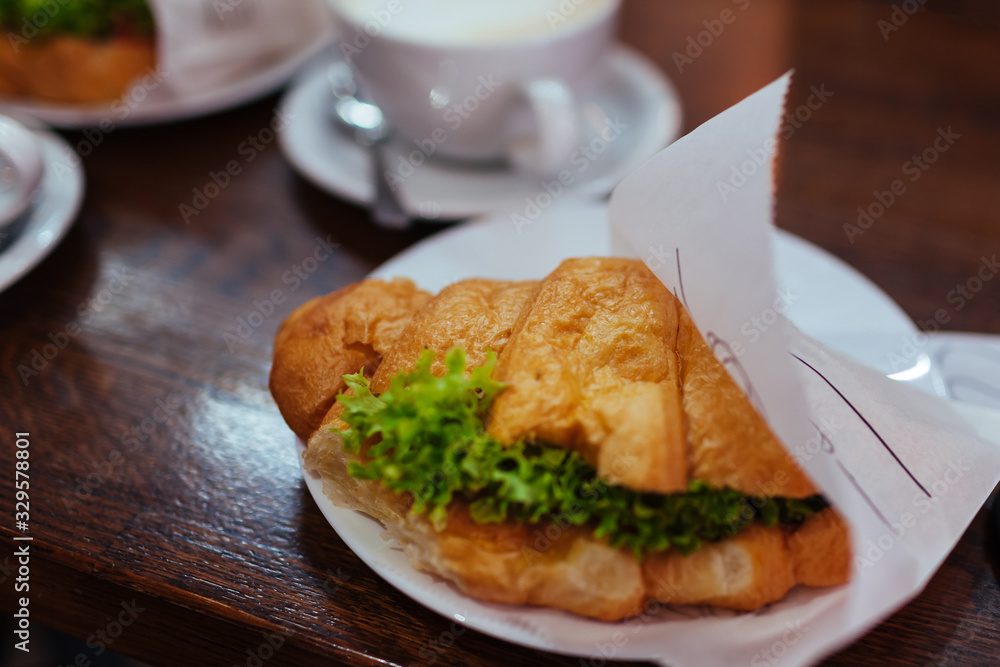 Croissant sandwiches and latte coffee served on cafe table. Breakfast with fresh bakery food and hot drink Croissant sandwiches and latte coffee served on cafe table. Breakfast with fresh bakery food and hot drink
