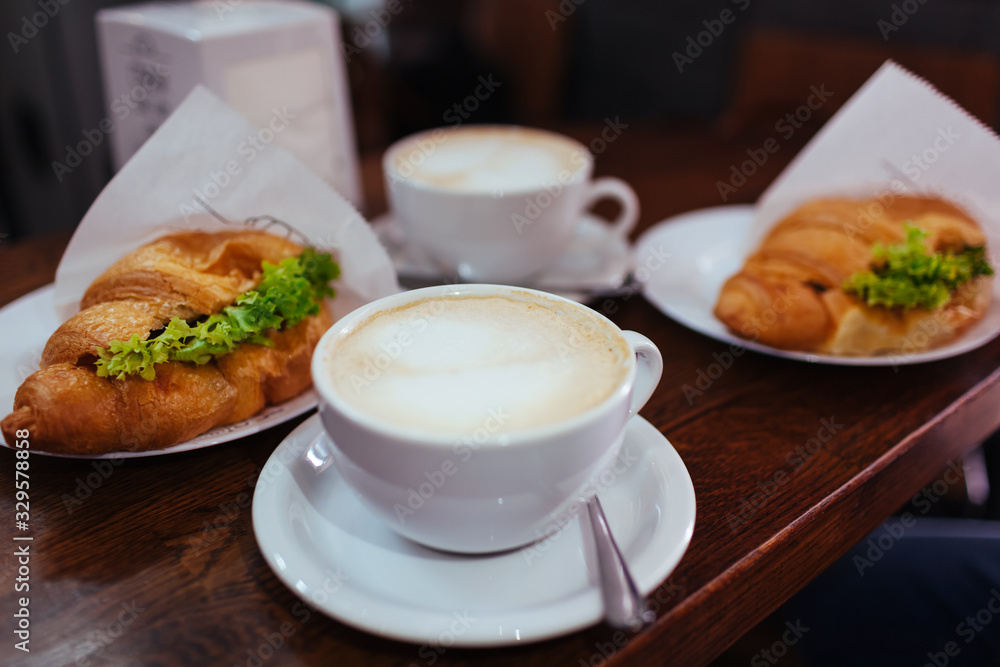 Croissant sandwiches and latte coffee served on cafe table. Breakfast with fresh bakery food and hot drink