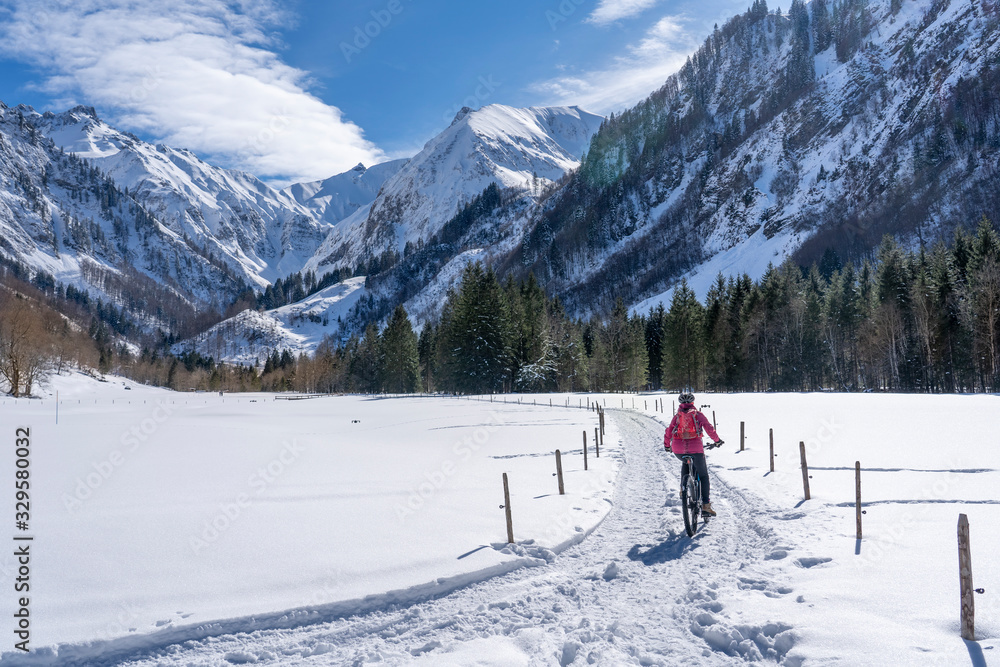 nice senior woman riding her electric mountainbike on a sunny winter day in the Allgau alps near Oberstdorf, Bavaria, Germany
