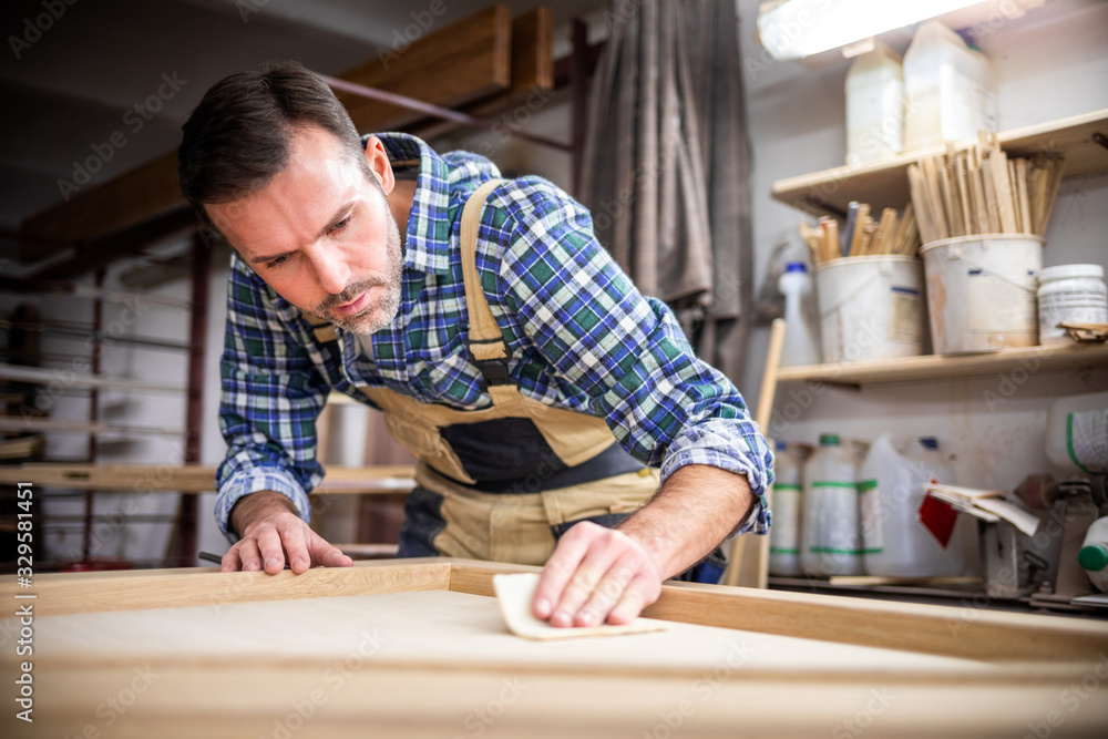 Professional carpenter polishing wood using abrasive paper in carpentry workshop Professional carpenter polishing wood using abrasive paper in carpentry workshop