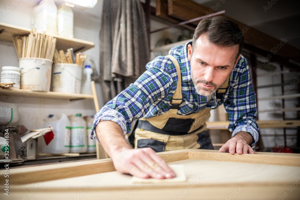 Professional carpenter polishing wood using abrasive paper in carpentry workshop Professional carpenter polishing wood using abrasive paper in carpentry workshop